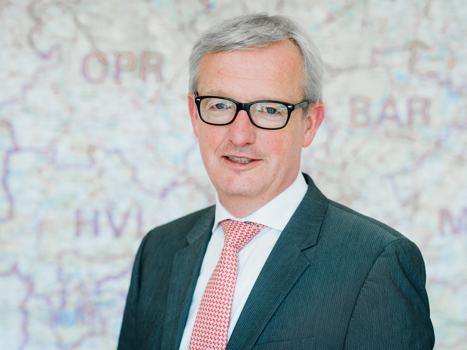 Portrait von Guido Beermann: grauhaariger Mann, schwarze Brille, Anzug, rosa Krawatte.