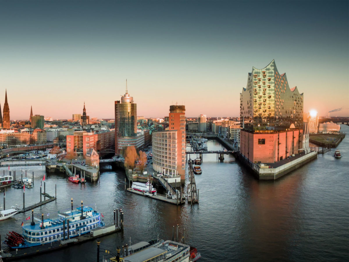 Das Titelbild zum Beitrag "Entwicklung der Baubranche in der Metropolregion Hamburg" zeigt die Stadt aus Richtung der Elbe bei Sonnenaufgang.