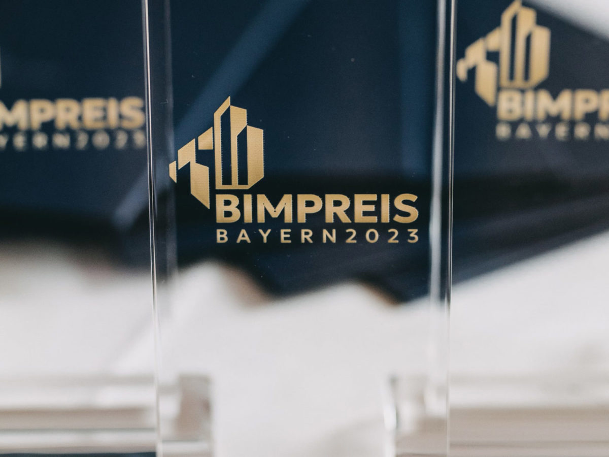 Detailaufnahme einer BIM-Preis Trophäe. Sie ist durchsichtig und trägt in gold die Aufschrift "BIMPREIS Bayern 2023". Die STRABAG AG wurde ausgezeichnet.