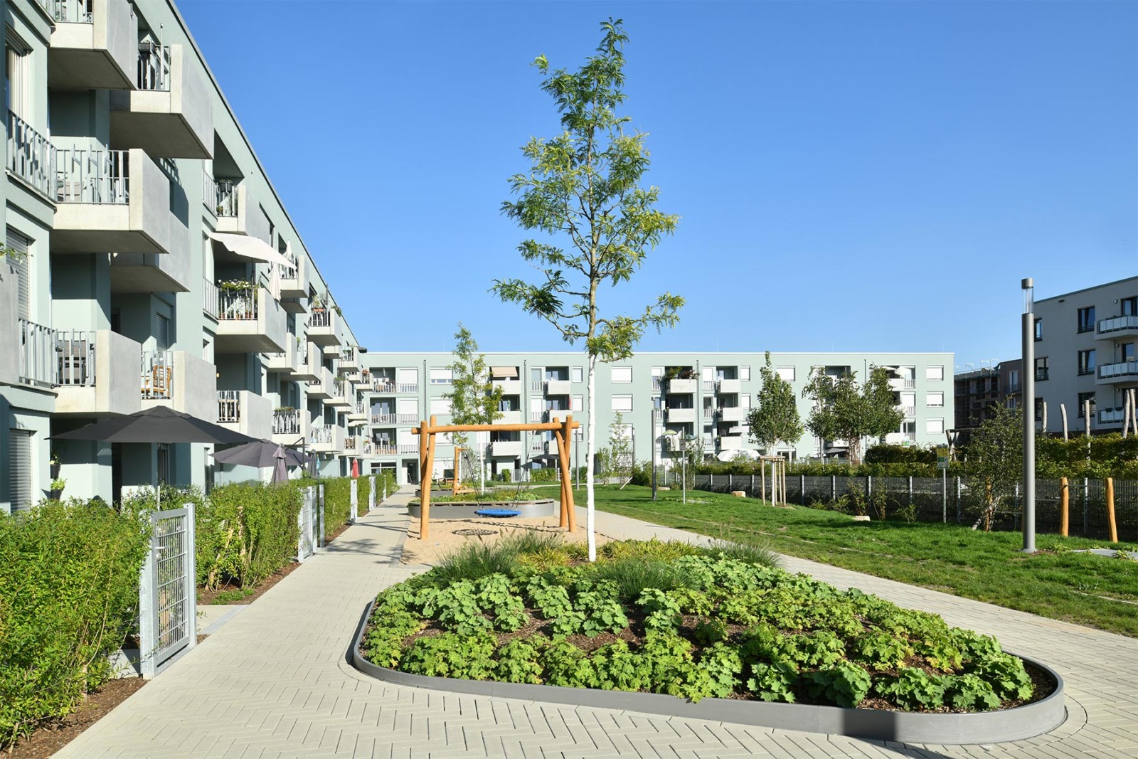 L-förmiges Clouth-Quartier in Köln. 4 Geschosse, grün-blaue Fassade, begrünter Innenhof mit Spielplatz.