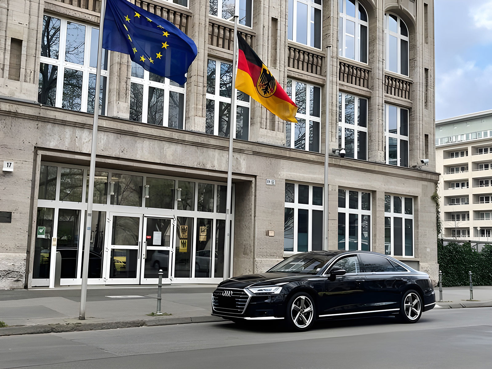 Ein Audi steht vor einem Regierungsgebäude. Draußen sind die Deutschlandflagge und die Europaflagge gehisst