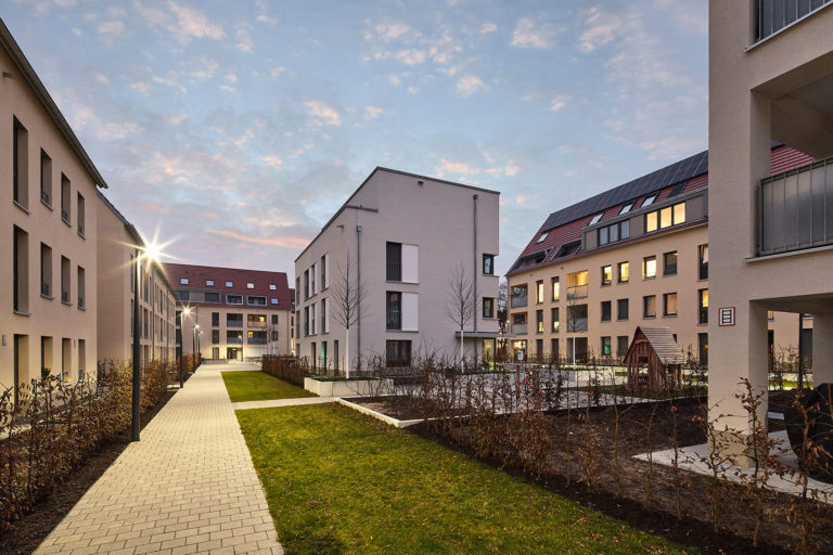 Foto der Wohnsiedlung in der Düsseldorfer Straße Stuttgart. Ein Gehweg verläuft neben Grünflächen zwischen Gebäuden hindurch.