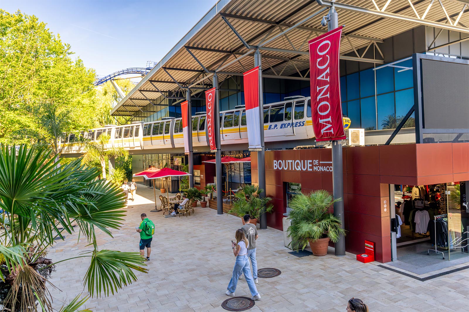 Monorail-Bahn im Europa-Park schwebt über der Boutique de Monaco zwischen Palmen und roten Monaco-Bannern
