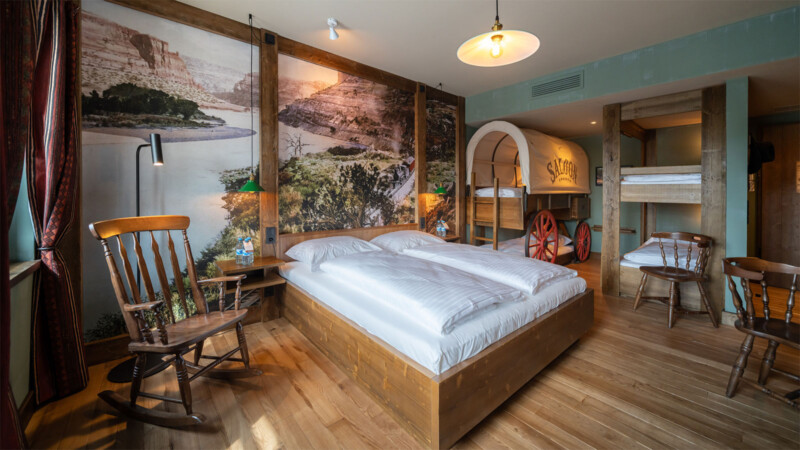 Gemütliches Themenzimmer der Riverside Western Lodge mit Planwagen-Bett und rustikaler Wanddekoration