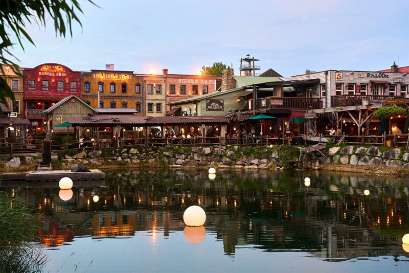 Beleuchtete Saloon- und Ladenfassaden der Silver Lake City spiegeln sich abends im Wasser