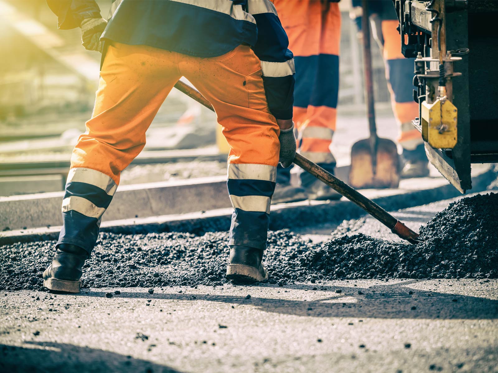 Die Elbchaussee in Hamburg wird ab 2025 grundsaniert. Das Bild zeigt einen Bauarbeiter, der Asphalt auf eine Straße schaufelt.
