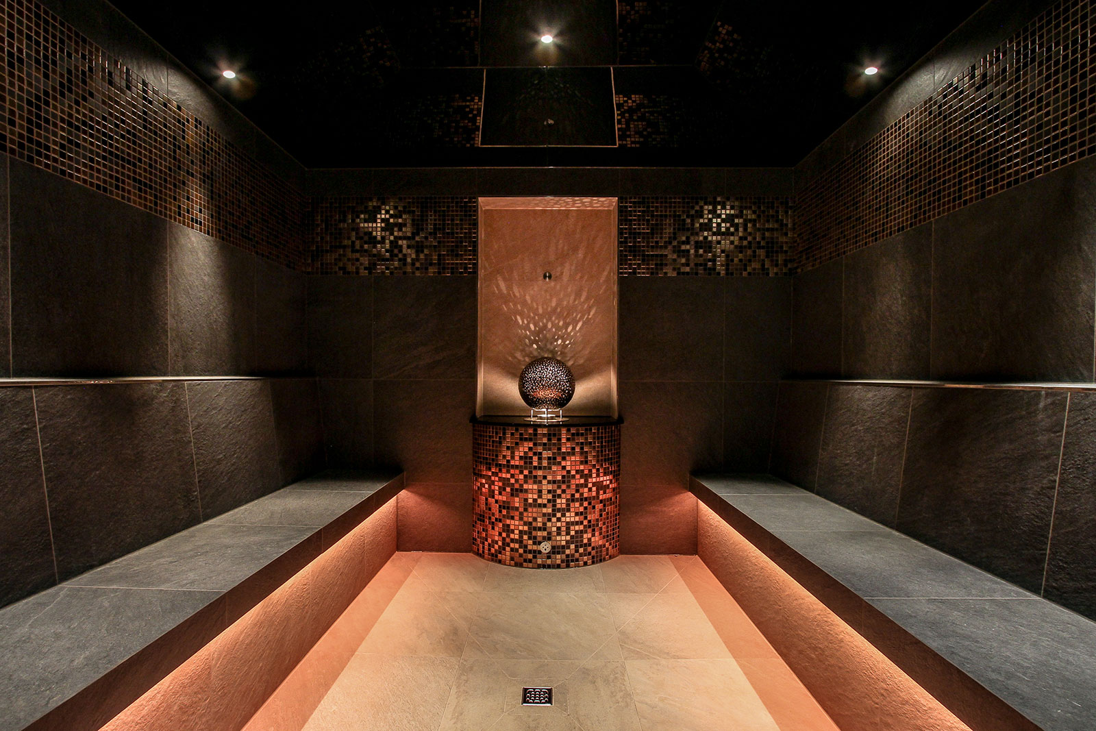 Profilbild der KLAFS GmbH: Foto einer sehr hochwertigen Sauna mit dunkelgrauen Steinwänden. Der Boden ist hell und rot beleuchtet.