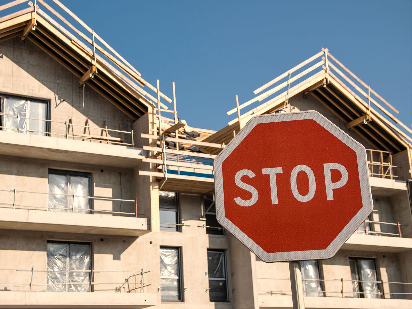 Haus mit Baugerüst im Hintergrund. Stopschild im Vordergrund symbolisiert den Fördermittelstop für das Förderprogramm Klimafreundlicher Neubau.