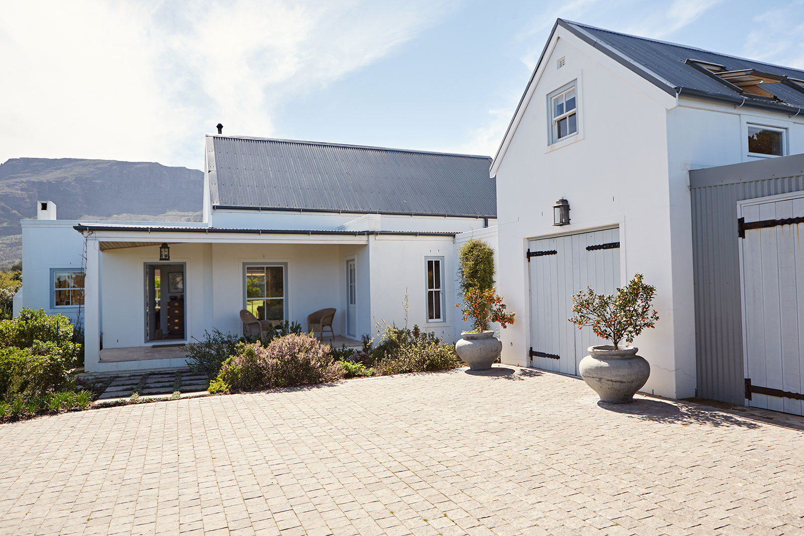 Weiß gestrichenes Wohnhaus mit grauem Dach, Garage und gepflastertem Hof