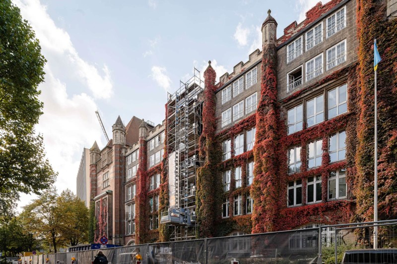 Foto des denkmalgeschützten alten Fernmeldeamts, das zum Campus Schlüterstraße umgebaut wird. An der Fassade ranken rote Kletterpflanzen.