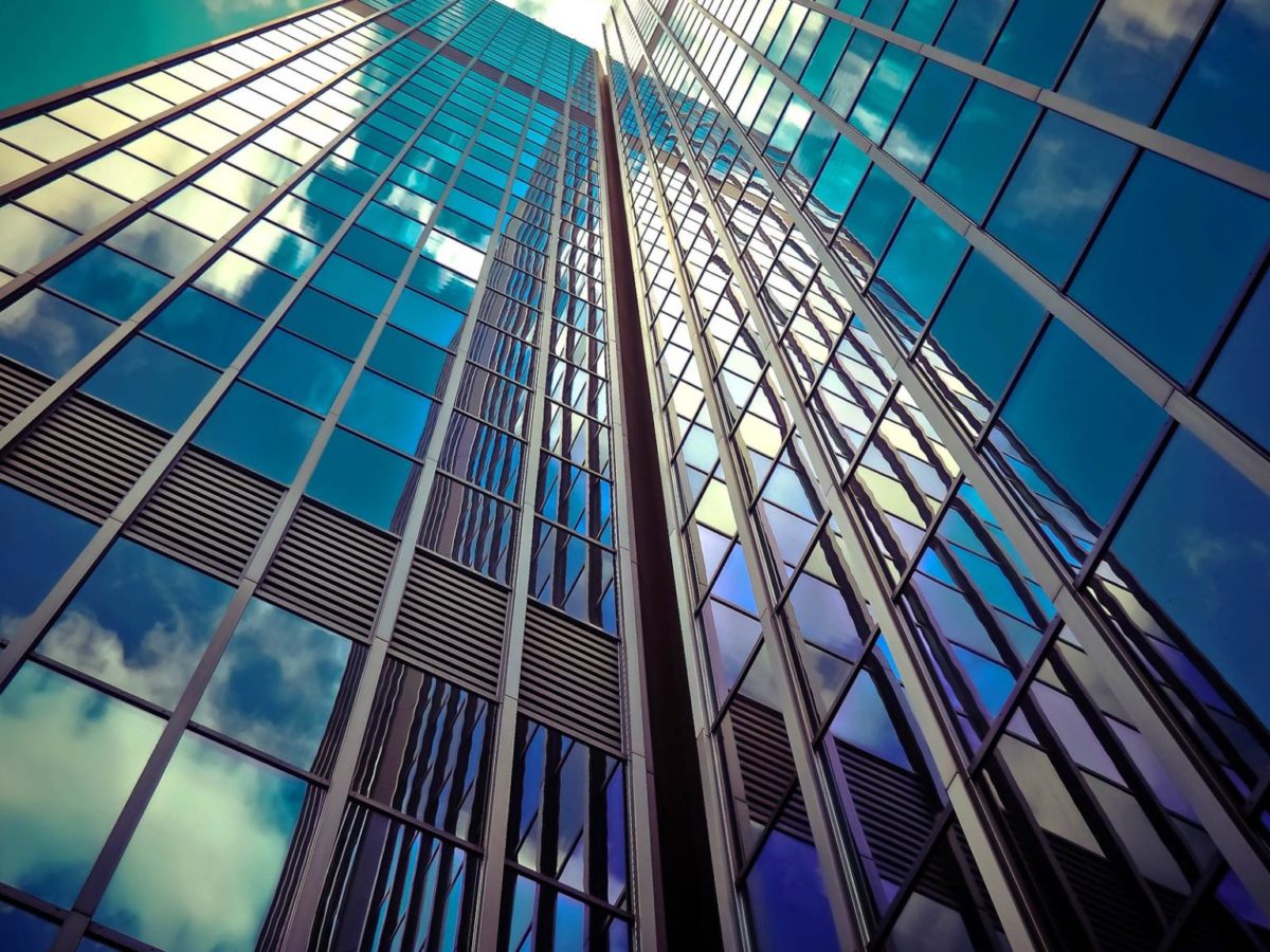 Auf dem Bild zum Beitrag Meine Stadt der Zukunft ist ein Wolkenkratzer mit moderner Glasfassade von unten zu sehen. Die Wolken und der Himmel spiegeln sich in weiß und blau im Glas.