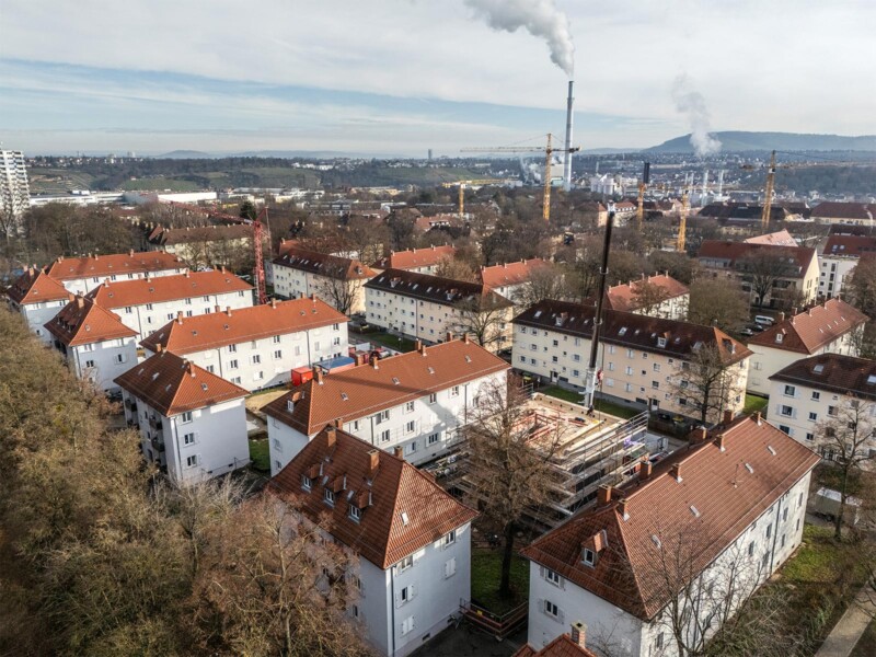 Luftaufnahme einer Wohnsiedlung mit Walmdächern und einer Baustelle mit Kran zwischen den Bestandsgebäuden