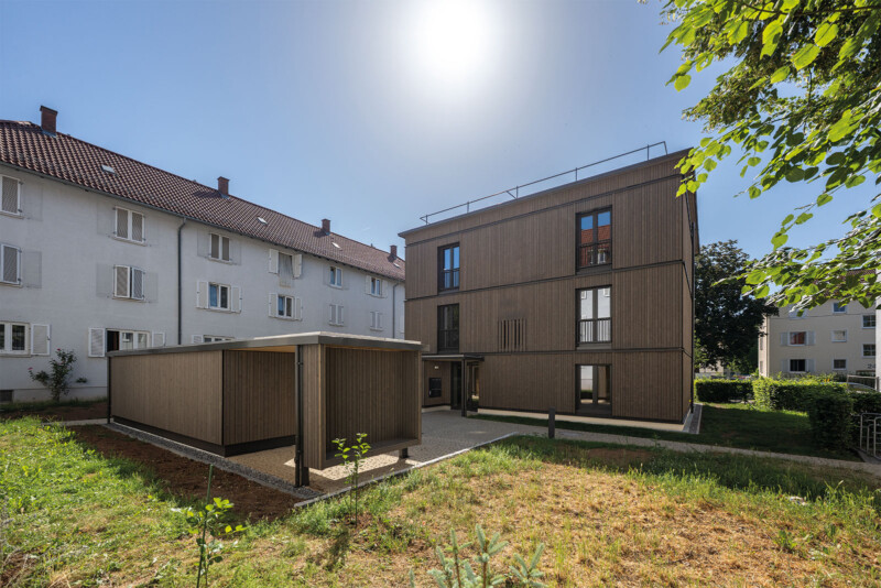 SWSG_EQ¹²: Fertiggestelltes Holzgebäude mit Dachterrasse und überdachtem Fahrradunterstand im Grünen