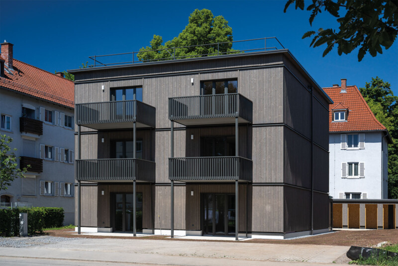 Dreigeschossiges Wohngebäude mit Holzfassade, Balkonen und Dachterrasse zwischen Bestandsbauten