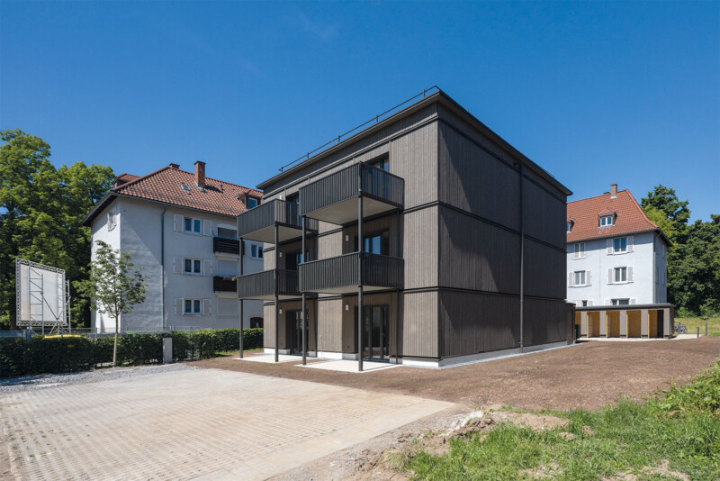 Seitenansicht eines Wohnhauses mit Holzfassade, Balkonen und angrenzendem Carport