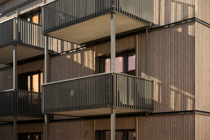 SWSG_EQ¹²: Nahaufnahme der Balkone und Holzfassade mit warmem Lichteinfall am Abend