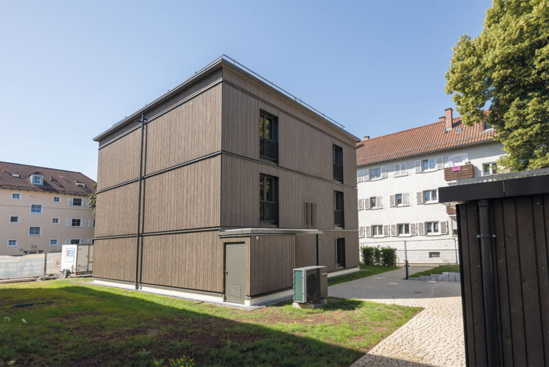 Rückansicht eines Holzgebäudes mit Wärmepumpe und gepflastertem Zugangsweg