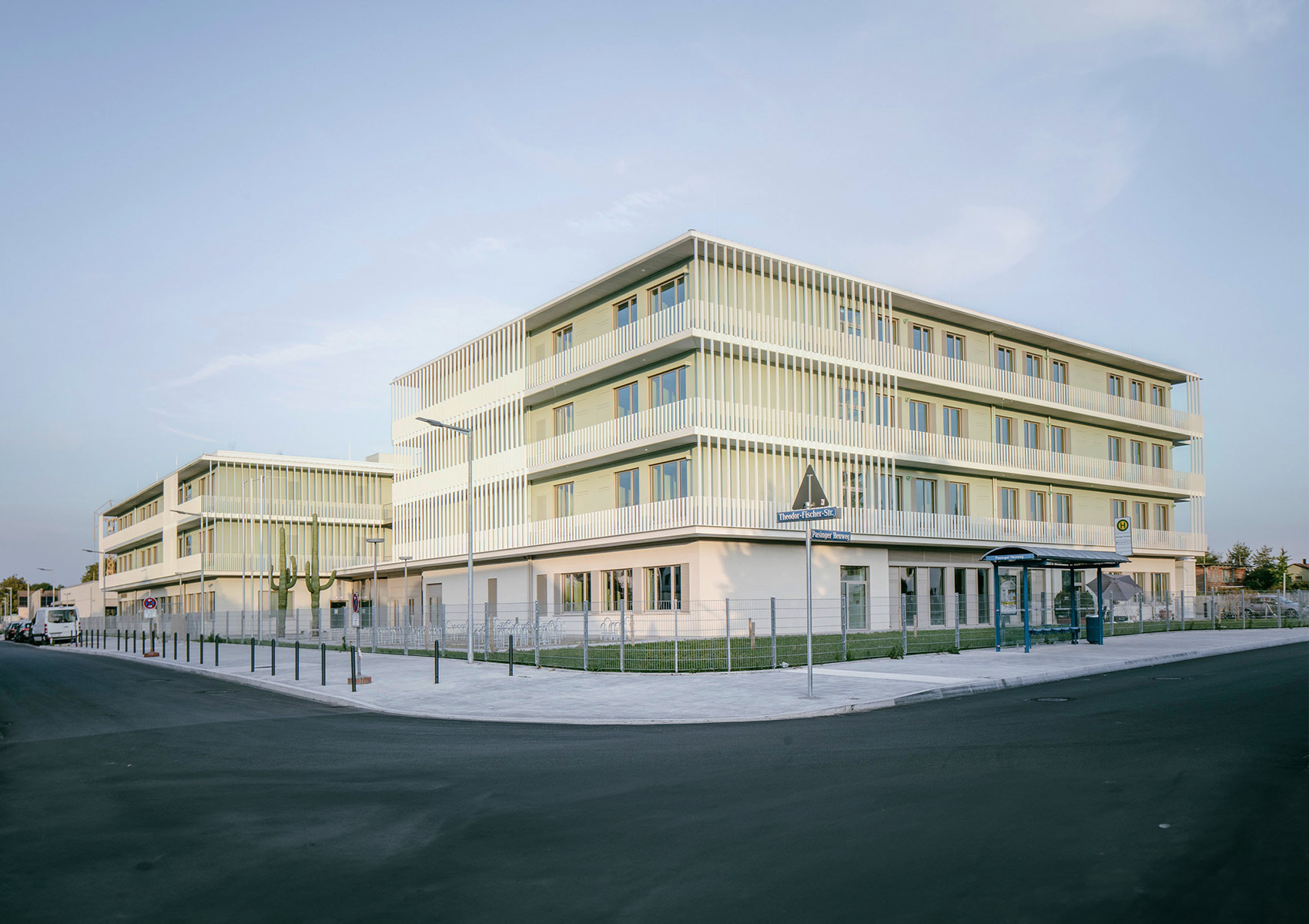 Die fertige Grundschule an der Theodor-Fischer-Straße in München. Im Vordergrund ist eine frisch asphaltierte Straße. In der Mitte des Bildes ist der vierstöckige Neubau.